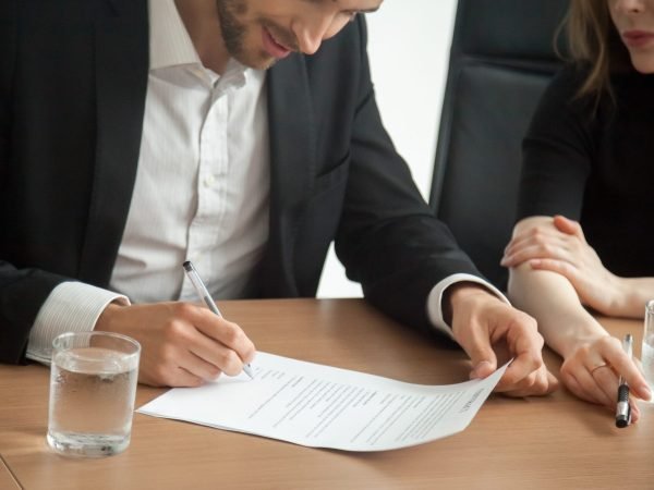 Satisfied smiling businessman in suit signing contract at meeting concept, investor or entrepreneur putting written signature on business document making good partnership deal, taking loan insurance
